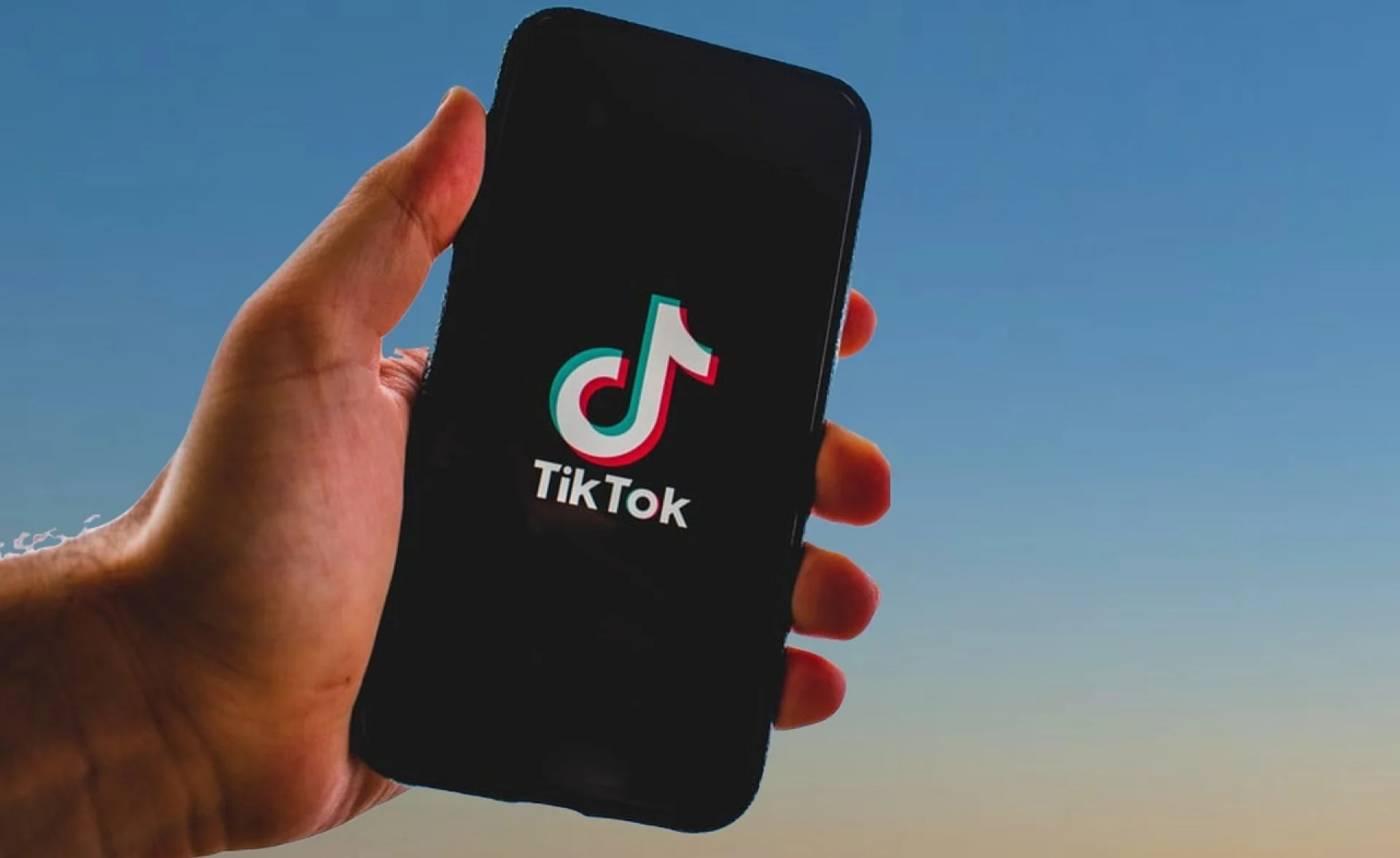 Mão segurando um celular que contém o logo do tiktok. O logo é preto e branco