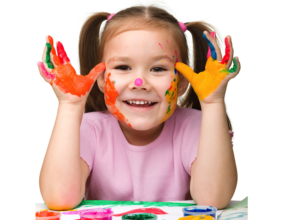 Imagem de uma criança, com as mãos pintadas, sorrindo para a câmera